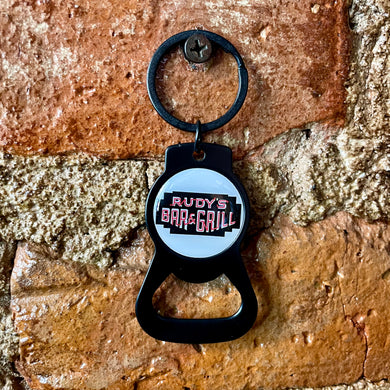 Rudy’s Bar & Grill keychain bottle opener displayed flat on a classic brick surface